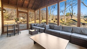 A covered outdoor seating area with a sofa, a table, and a small kitchen setup. - Whispering Brook-Outdoor oasis w/stream-Sleeps 16 (Springdale)