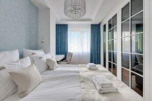 A hotel room with a large bed, a desk, and a view through floor-to-ceiling windows. - Seaside Primore by Downtown Apartments (Gdansk)