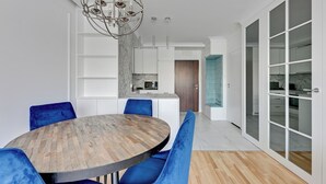 Een moderne eetruimte met een ronde houten tafel, blauwe fauteuils en een kroonluchter.