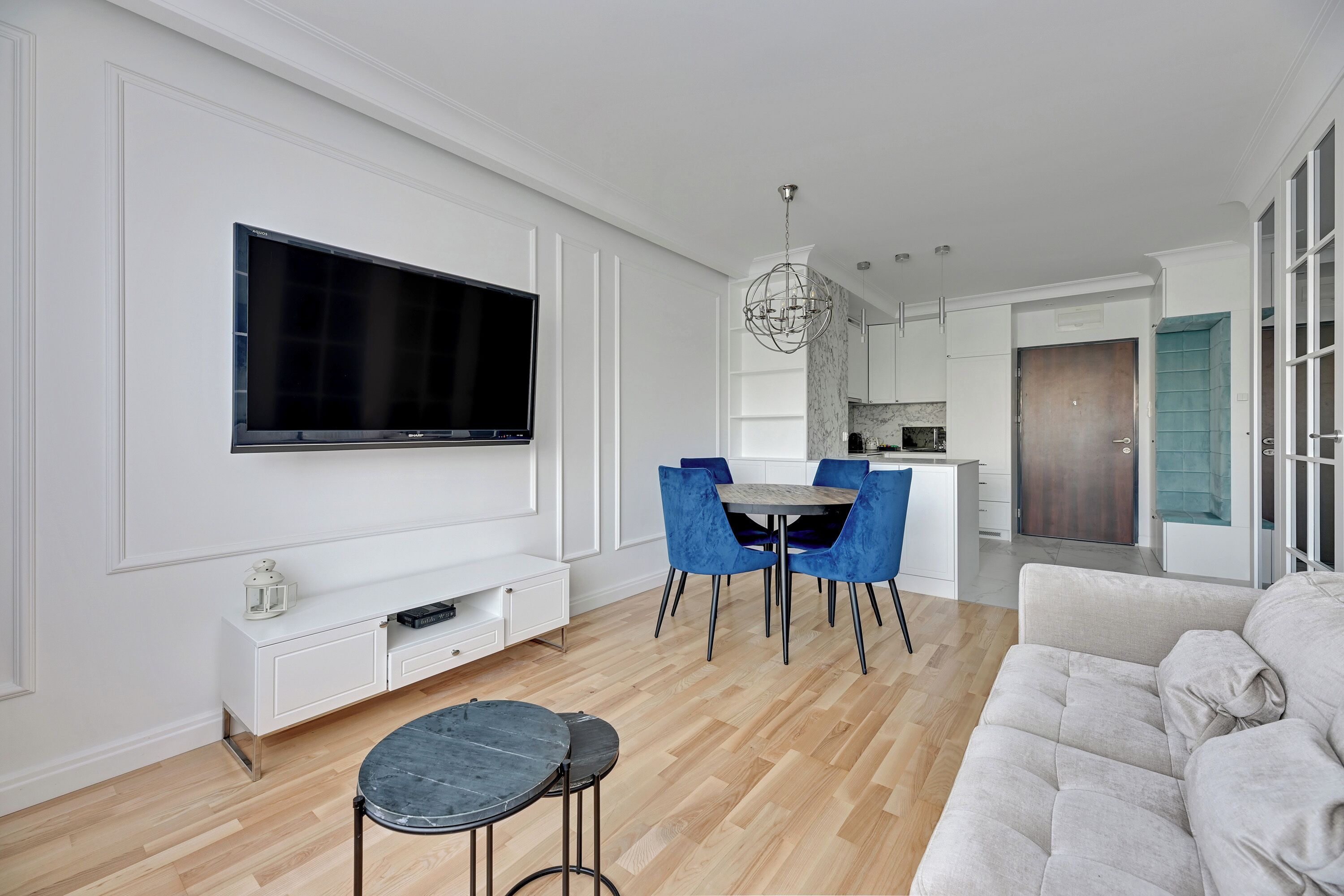 Ein modernes Wohnzimmer mit Flachbildfernseher, Essbereich mit blauen Stühlen und einer Couch.