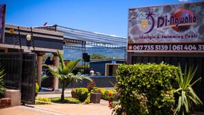 Un edificio con un letrero que dice 'Di-NgWako Lifestyle & Swimming Pools' y números de contacto.