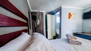 Habitación de hotel con cama, ventilador, baño a la vista a través de una puerta abierta y un cuadro en la pared.