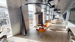 A spacious, modern lounge area with a high ceiling, large windows, and a view of the cityscape. - Student Only Shoreditch (London)