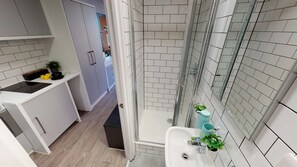 Un baño moderno con cabina de ducha de vidrio, un lavabo con un florero azul y una encimera blanca con una tetera y limones.