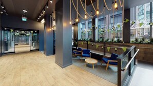 A modern lobby with wooden flooring, blue seating, and hanging lights. - Student Only Shoreditch (London)