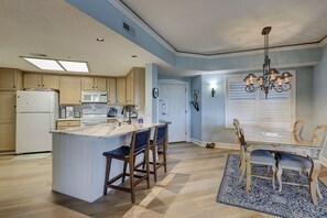 A kitchen with a central island, wooden chairs, a dining table with chairs, a chandelier, and a white door.