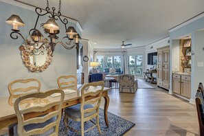 A dining area with a wooden table and chairs, a chandelier, and a large mirror with a seashell border.