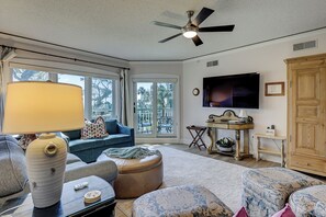 Sala de estar con ventilador de techo, televisor, sofá, mesa de centro y vistas a través de puertas de vidrio.