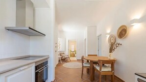 A modern kitchen with white cabinets, a built-in oven, and a stainless steel range hood. There is a dining area with a wooden table and chairs, and a small rug on the floor. - Ground floor apartment - Villa Natura Bliss (Alcácer do Sal)