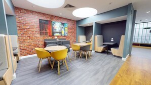 A modern interior with a brick wall, a round table with yellow chairs, and a seating area with cushioned benches. - Student Only Will Wyatt Court (London)