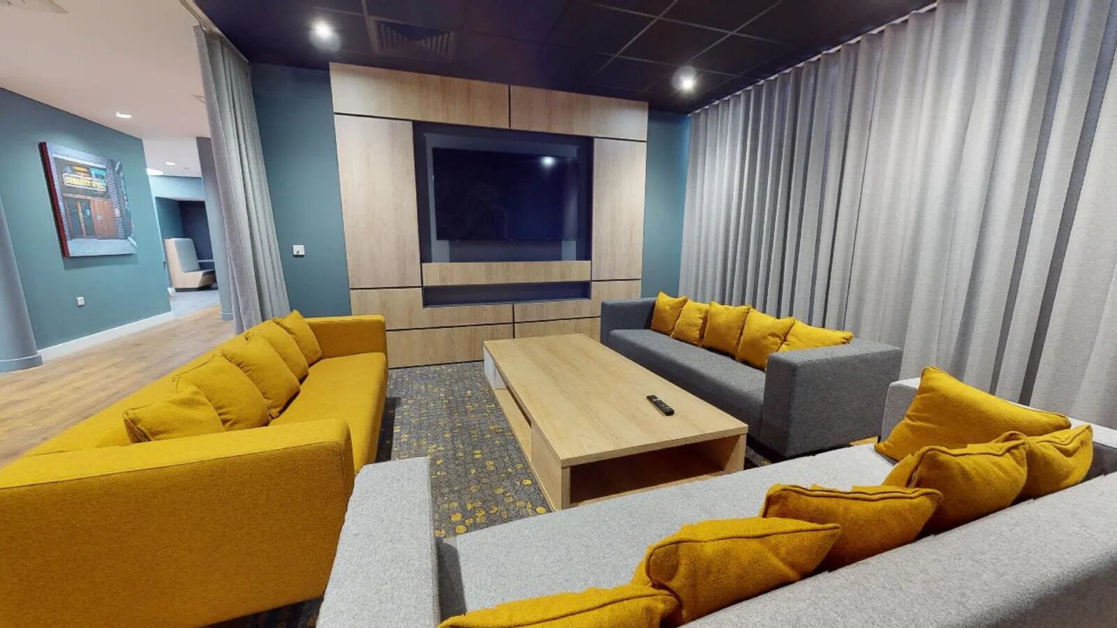 A modern living room with a large flat-screen TV, two sofas, a coffee table, and a grey couch.