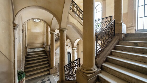 A grand staircase with ornate railings, leading to an upper level with arched ceilings and a checkered floor. - Palazzo Bicocca Rooms (Catania)