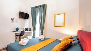 A hotel room with a bed, a desk with a chair, a television, and a mirror. - Palazzo Bicocca Rooms (Catania)
