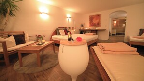 Une pièce agréable et bien éclairée, avec un lit, une table basse en bois, un vase blanc et une petite table sur laquelle se trouvent une bouteille et des fleurs.
