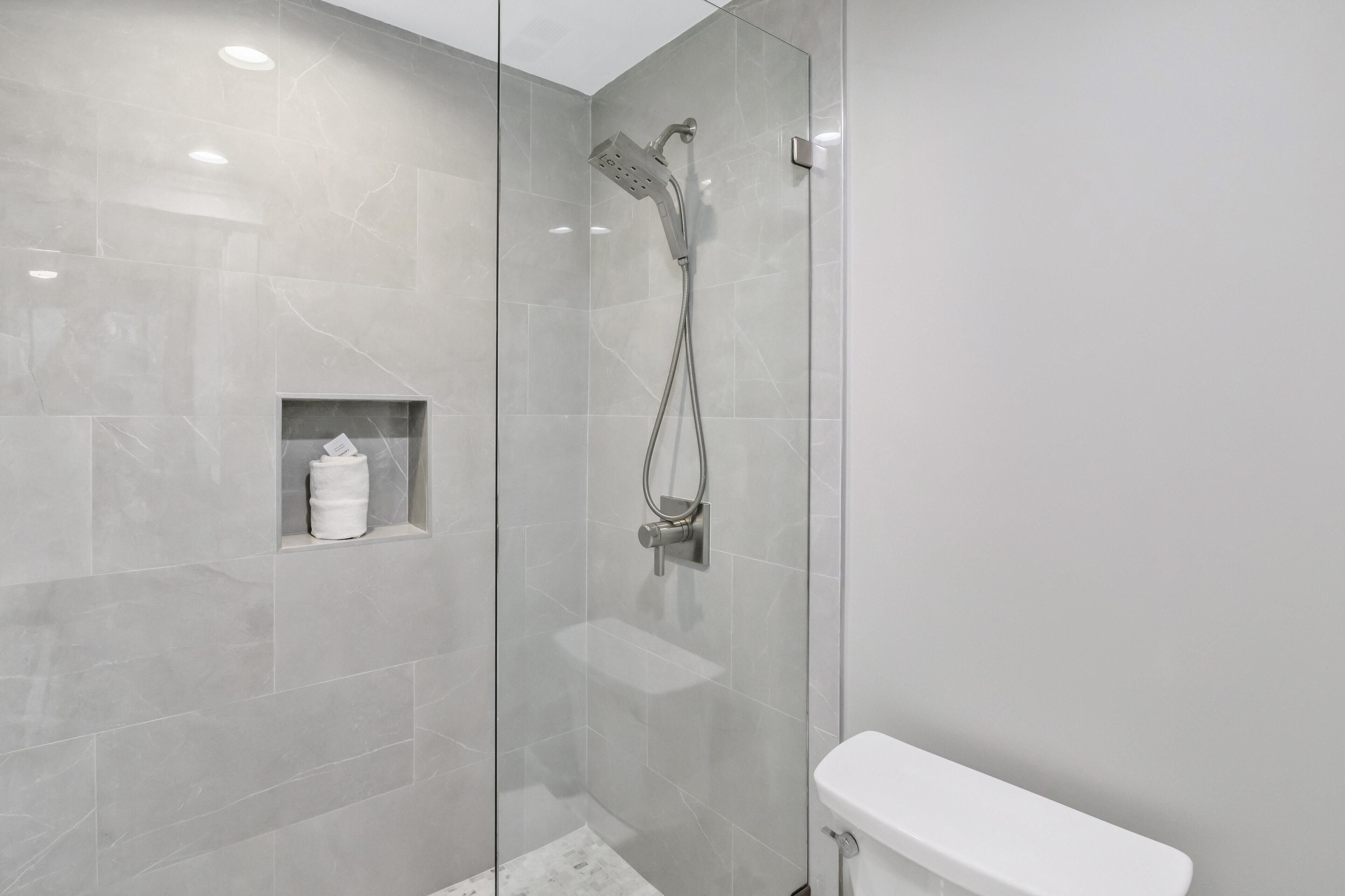 A modern bathroom with a glass-enclosed shower, a white toilet, and a small shelf with a towel.
