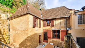 Un bâtiment en pierre avec un toit en tuiles, une table en bois entourée de chaises et un escalier menant à un étage supérieur.