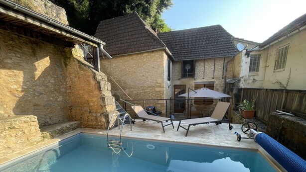 Une piscine avec un flotteur rose gonflable, une chaise longue et une petite table avec un ventilateur.