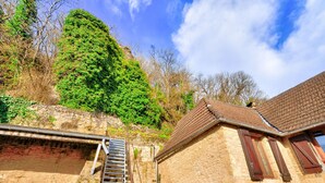 Un bâtiment en pierre avec un toit en tuiles, un escalier en bois et, en arrière-plan, une colline verdoyante.