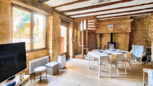 Une pièce rustique avec des poutres apparentes, une cheminée, une table à manger avec des chaises, un téléviseur et un radiateur.