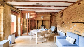Une pièce rustique avec des poutres apparentes, un mur en pierre, une table à manger avec des chaises, un canapé bleu et un petit radiateur.