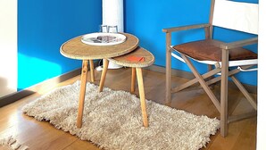 A room with a blue wall, a round table with a woven top, a chair with a white cushion, and a large window with a beige blind. - A bed and breakfast in the woods (Pommiers)