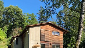 A two-story house with a deck, outdoor seating, and a tree in the foreground. - A bed and breakfast in the woods (Pommiers)
