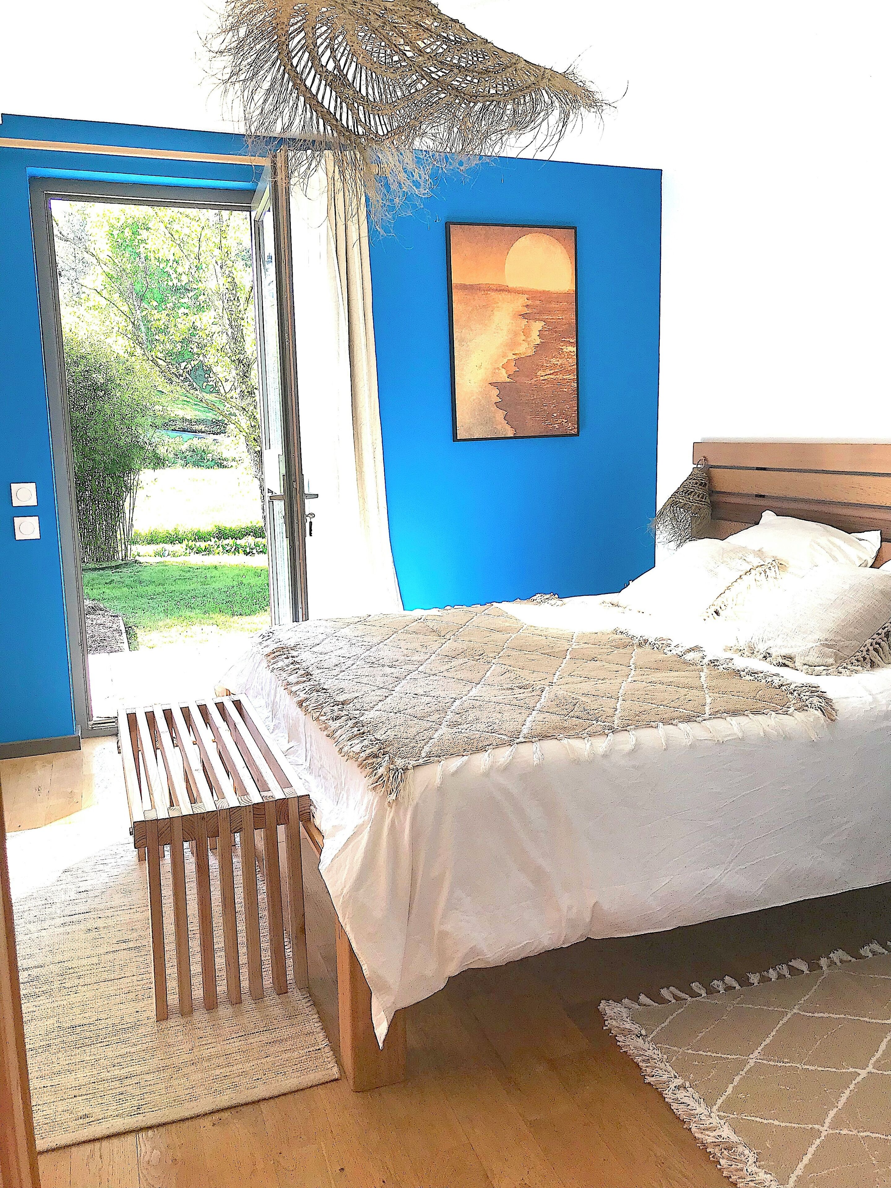 Un dormitorio con cama, un banco de madera, un cuadro y vistas a un jardín.