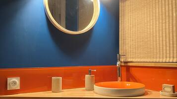 A bathroom with a round mirror, orange sink, and a wooden cabinet.
