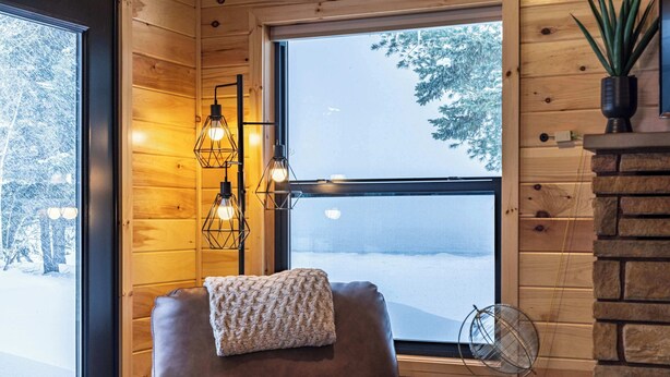 A cozy room with a leather chair, a knitted throw, a globe on a table, and a view of a snowy landscape through a large window. - Fall on Whitefish Bay | Private Beach, Fireplace (Paradise)