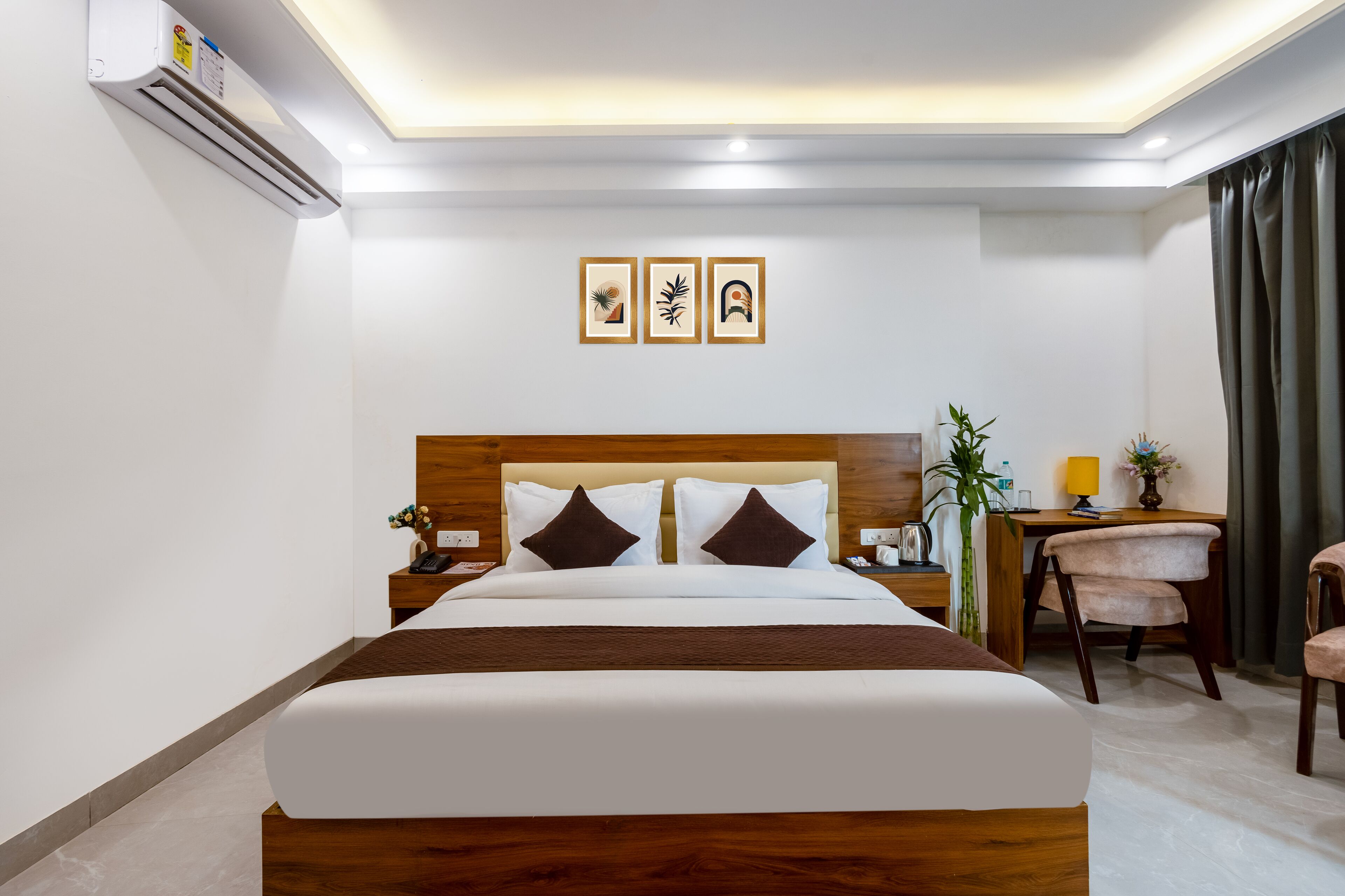 Ein Hotelzimmer mit einem großen Bett, einem Schreibtisch, einem Stuhl und einem kleinen Tisch. Über dem Bett hängen drei gerahmte Bilder an der Wand.