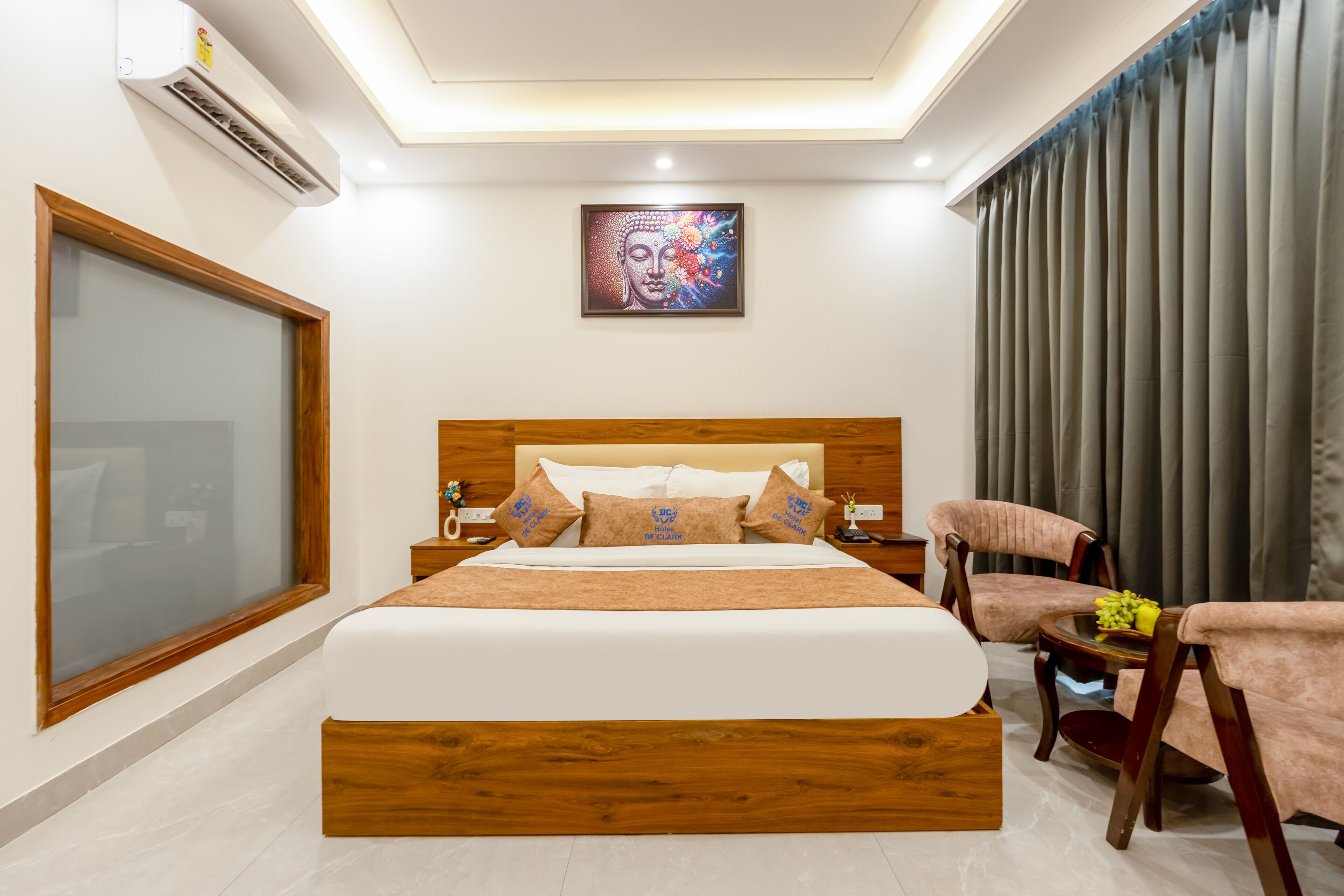 Habitación de hotel con una cama grande, cabecera de madera, un cuadro en la pared y vistas al exterior por la ventana.