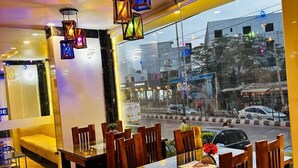 Un restaurante con mesas y sillas de madera, una partición de vidrio y faroles colgantes.
