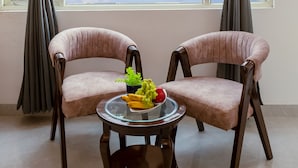 Una habitación con dos sillas, una mesita con frutero y una ventana con cortinas.