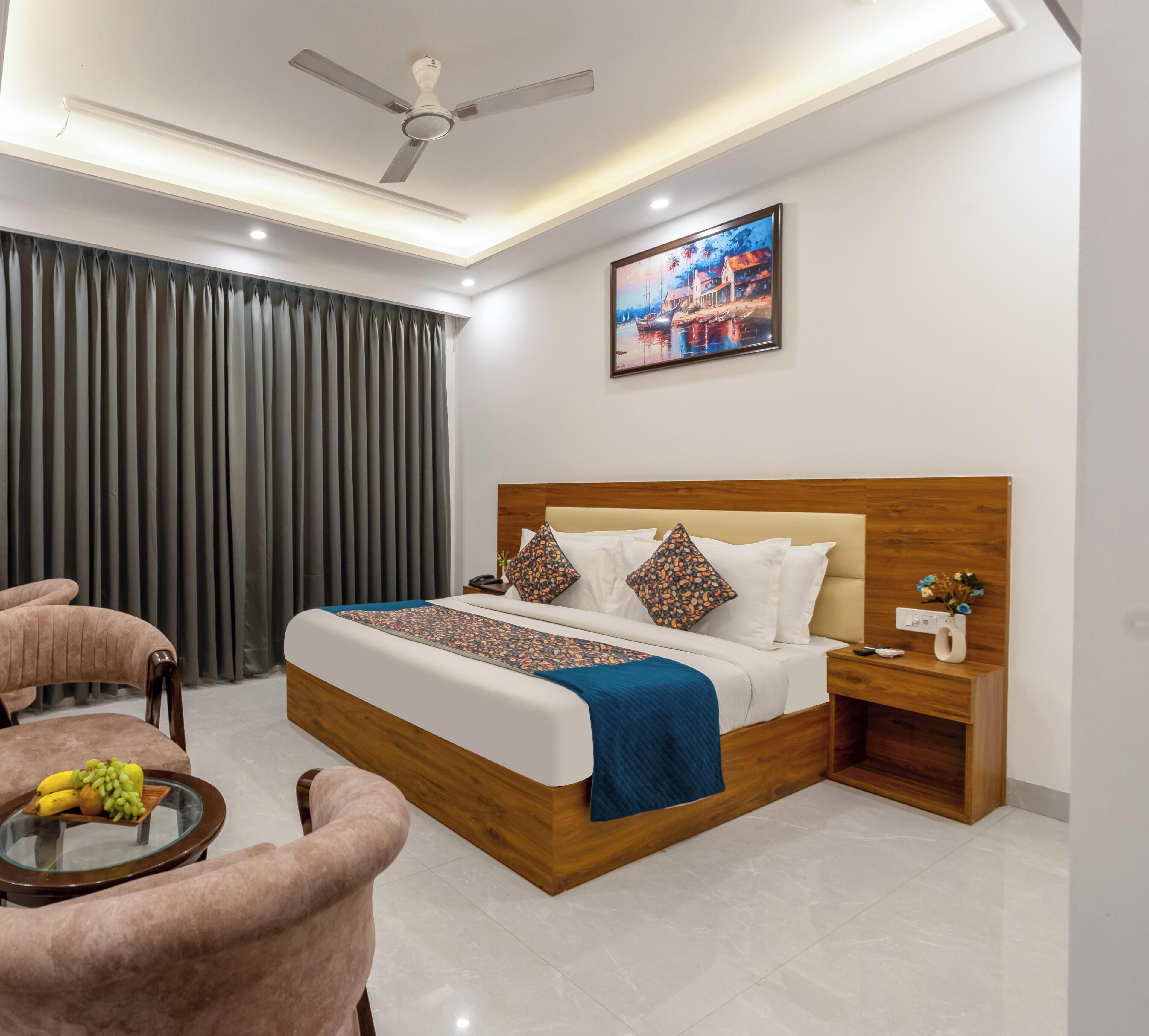 Habitación de hotel moderna con una cama, una mesita de noche, una silla, una mesa con fruta y un ventilador de techo.