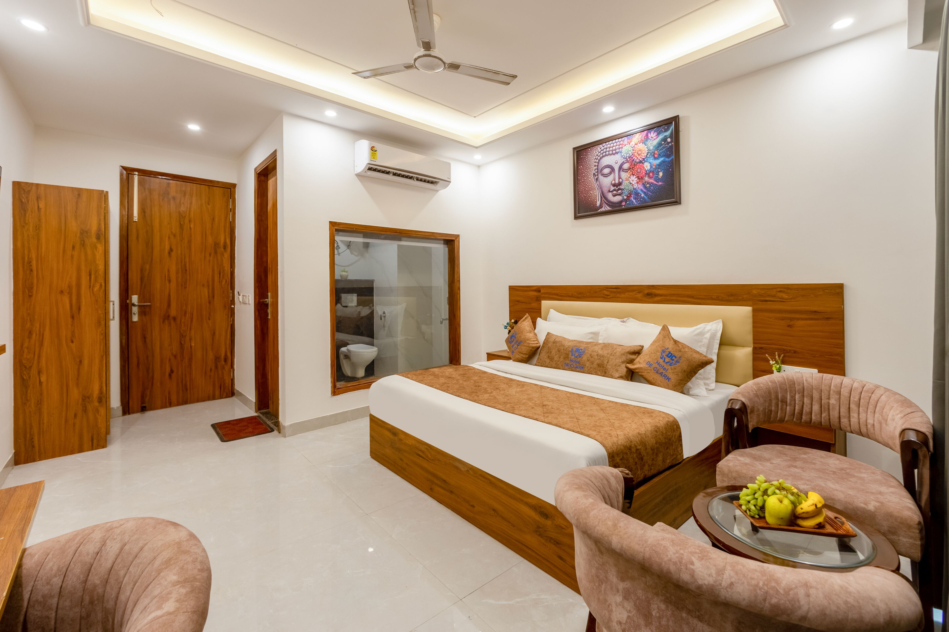 A hotel room with a bed, a chair, a small table with fruit, and a ceiling fan.