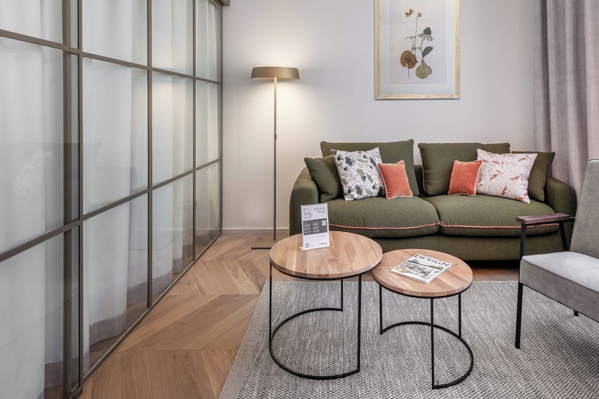A modern living room with a green sofa, two round tables, a floor lamp, and a framed botanical print on the wall.