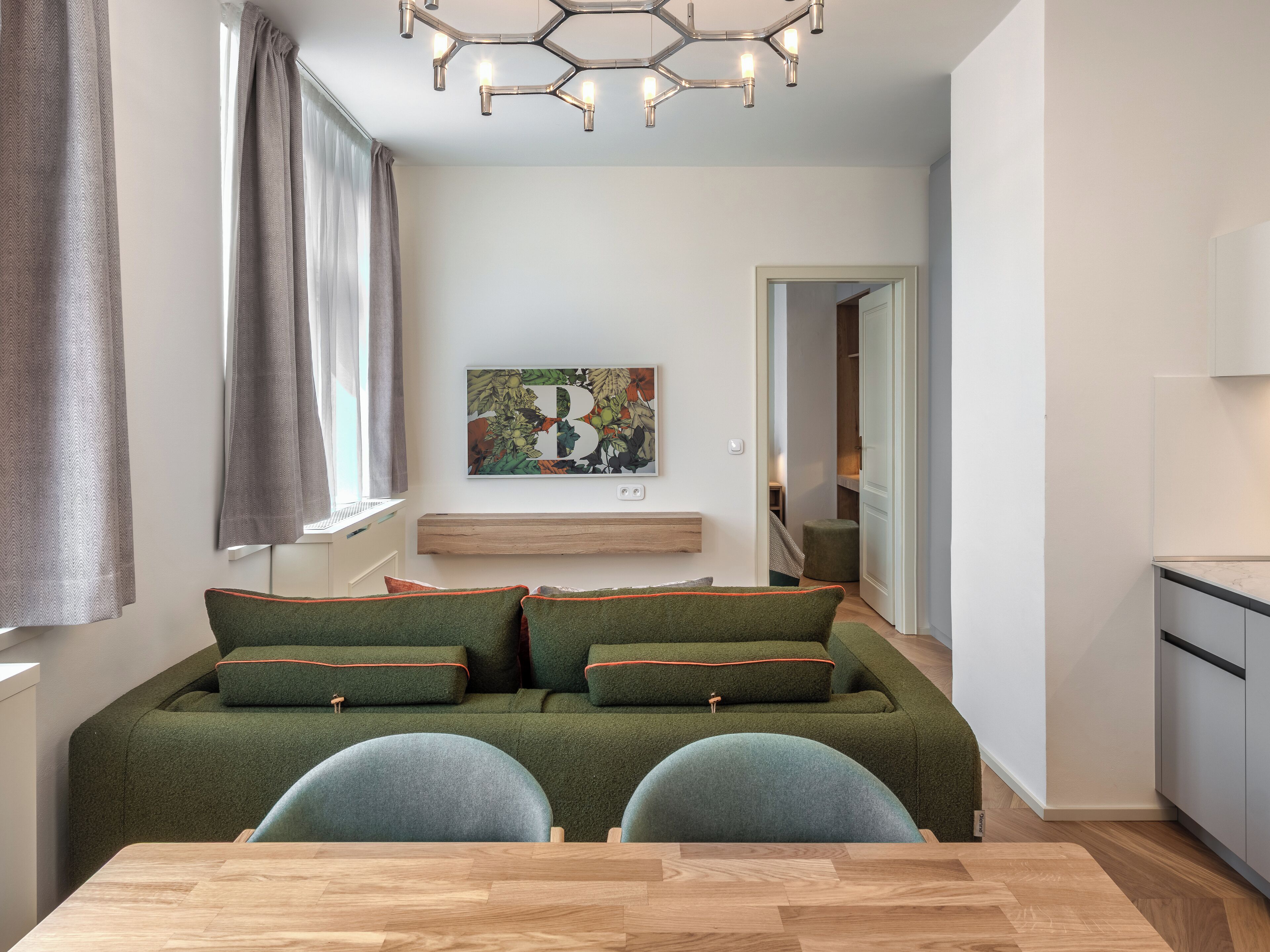 A modern living room with a sofa, two chairs, a wooden table, a ceiling light fixture, and a wall-mounted artwork.
