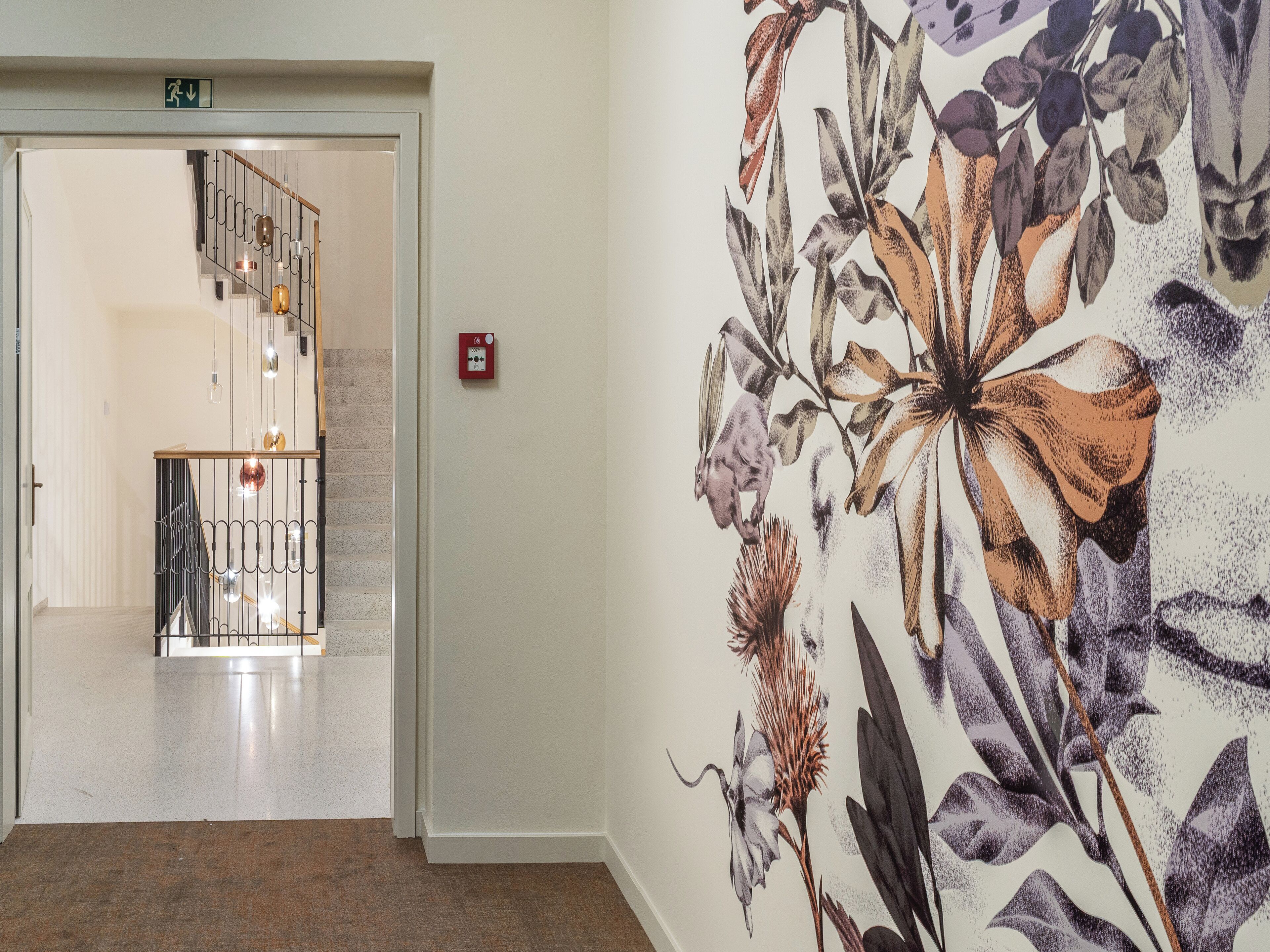 A hallway with a floral mural, a staircase, and a fire alarm.