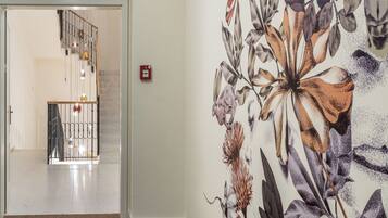 A hallway with a floral mural, a staircase, and a fire alarm.