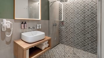 Un baño moderno con lavamanos blanco, tocador de madera y ducha con azulejos estampados.