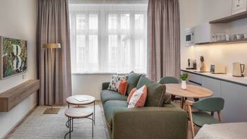 Una sala de estar moderna con un sofá verde, una mesa redonda de madera y una zona de cocina con microondas y tostadora.