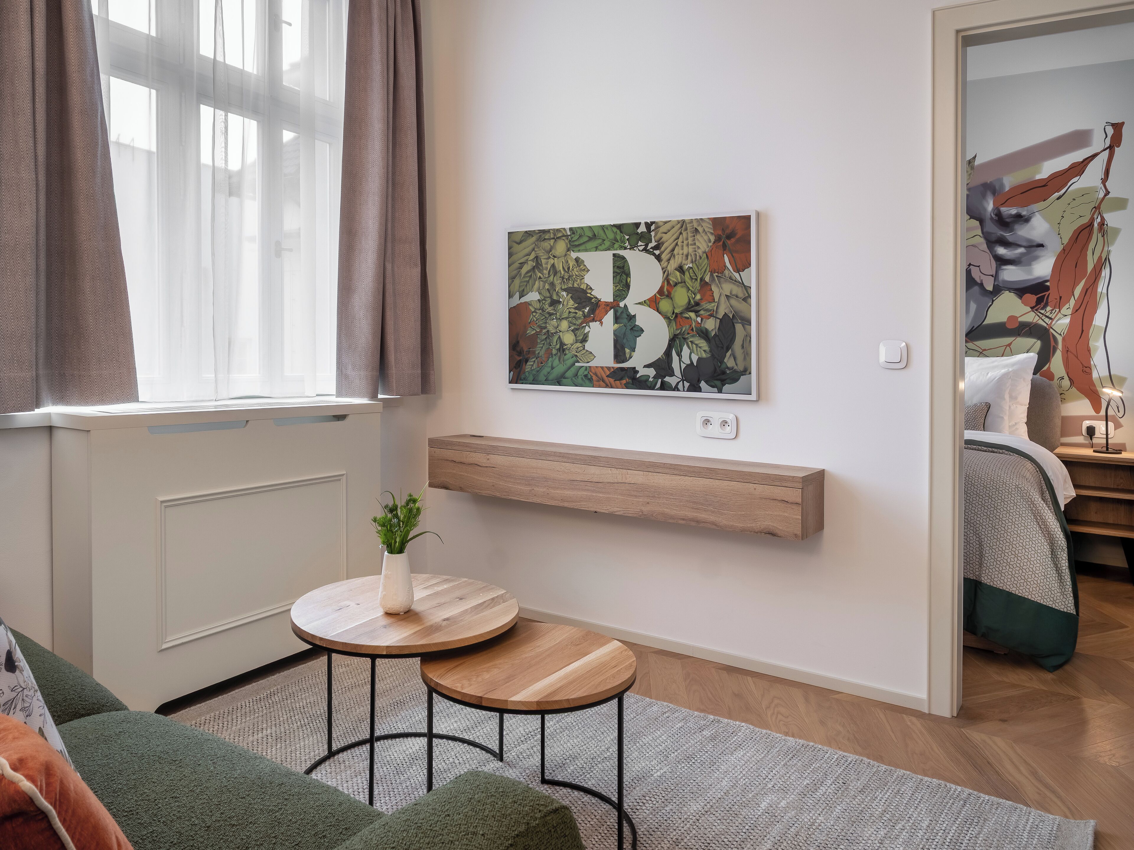Ein modernes Wohnzimmer mit großem Fenster, einem kleinen runden Tisch mit Pflanze, einem Wandbild und einem Holzregal.