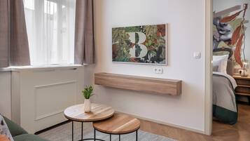 A modern living room with a large window, a small round table with a plant, a mounted artwork, and a wooden shelf.
