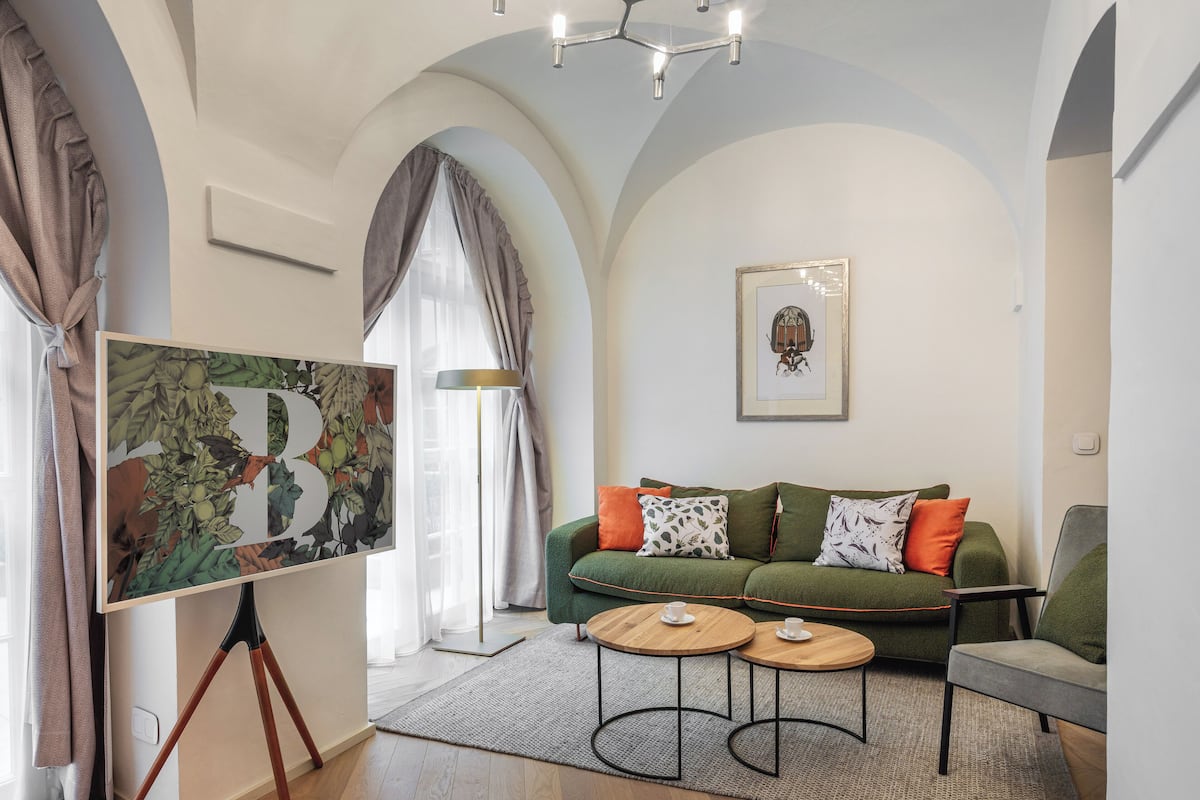 A modern living room with a green sofa, two round wooden tables, and a large framed artwork on the wall.