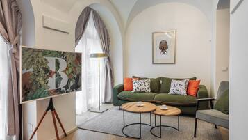 A modern living room with a green sofa, two round wooden tables, and a large framed artwork on the wall.