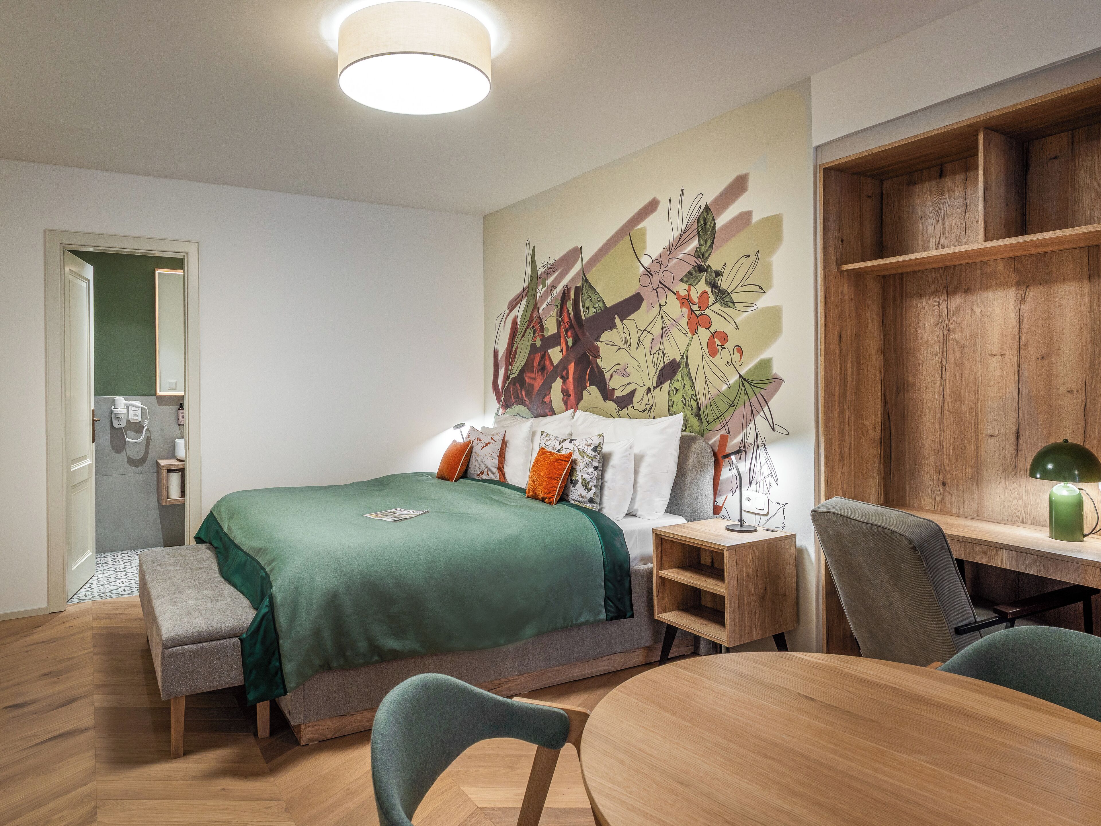 A modern hotel room with a bed, a desk, a chair, and a wooden shelf.