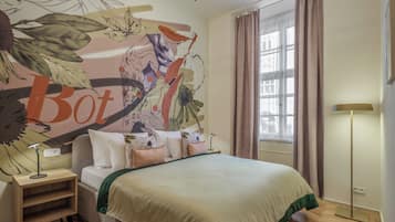 Un dormitorio con una cama grande, una mesita de noche, una lámpara, una ventana con cortinas y un mural en la pared.
