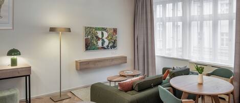 Una stanza moderna e luminosa con un divano verde, un tavolo rotondo e un quadro appeso al muro.
