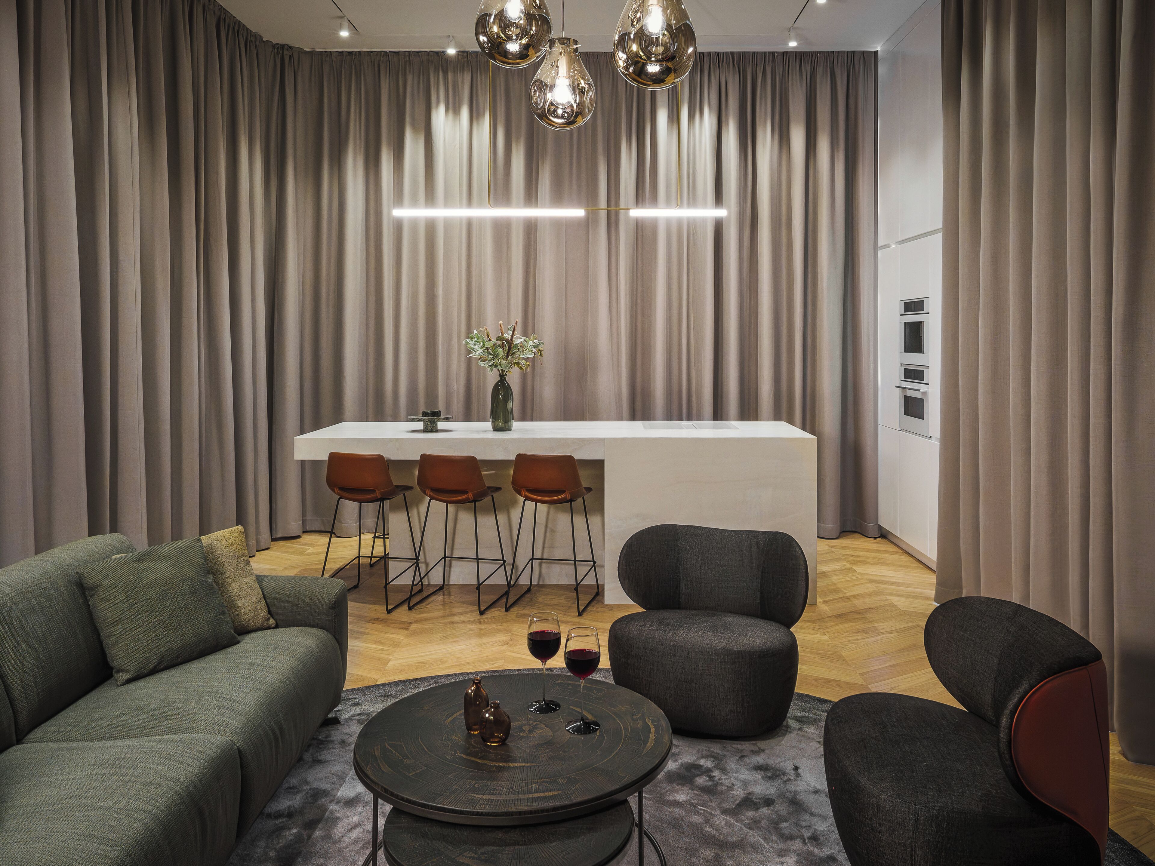Ein modernes Wohnzimmer mit einer Couch, Sesseln, einem Couchtisch und einem Essbereich mit Barhocker.