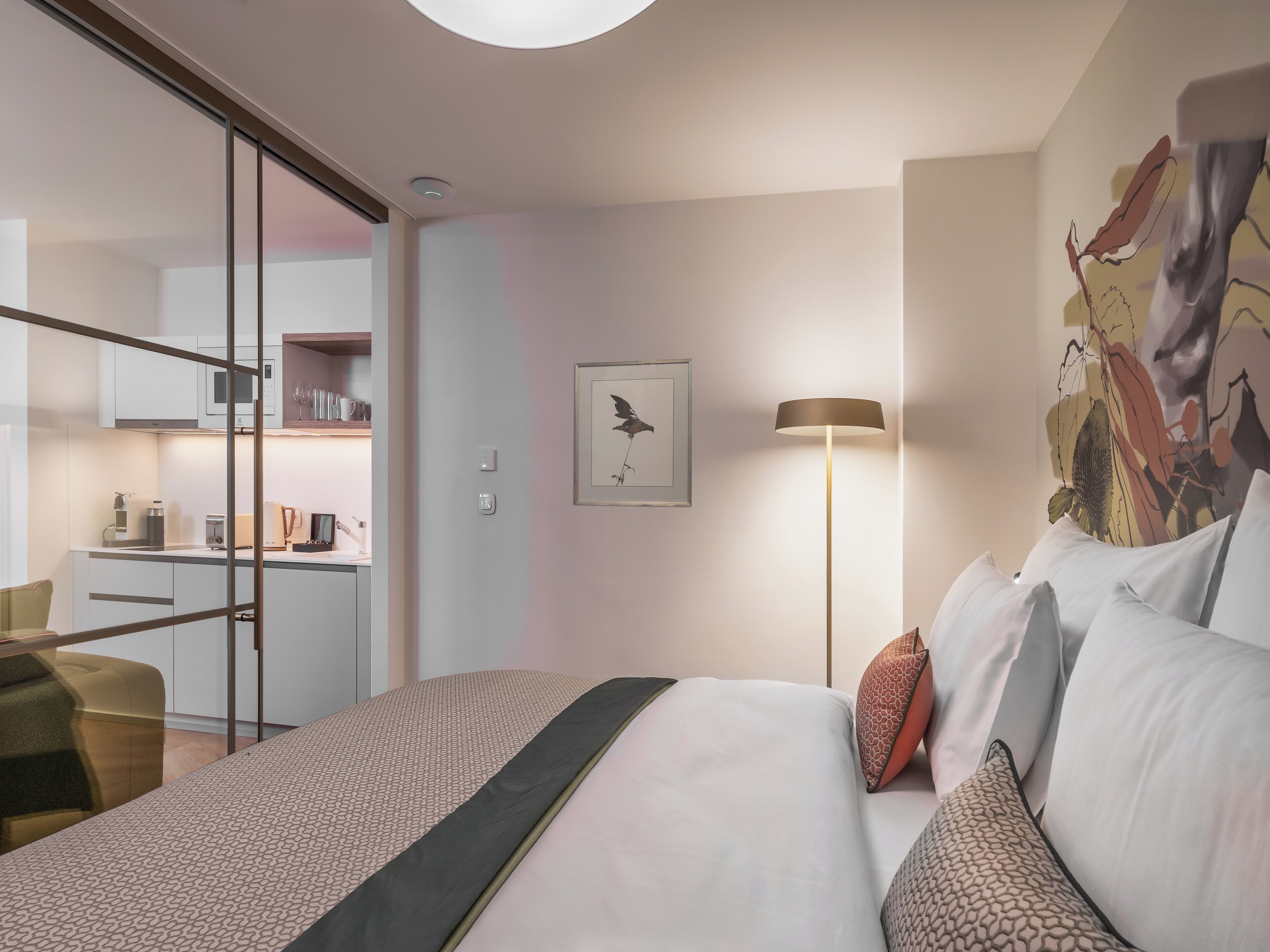 Une chambre d’hôtel moderne, équipée d’un lit, d’une table de chevet, d’une lampe et d’une œuvre d’art au mur.